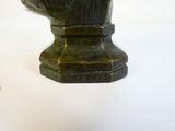 un vase vert avec un socle noir posé sur une table blanche