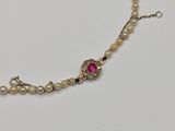 a close up of a necklace with pearls and a pink stone