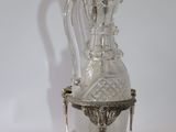 a glass bottle with a silver handle on a stand