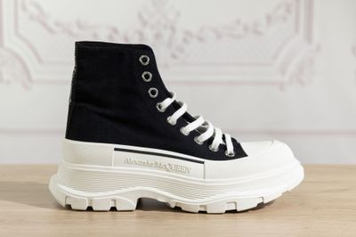 des baskets montantes noires et blanches à semelles blanches posées sur une table en bois