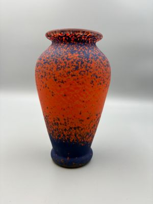 an orange and blue vase sitting on a white surface