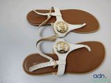 two pairs of white sandals with gold buckles on them on a white surface
