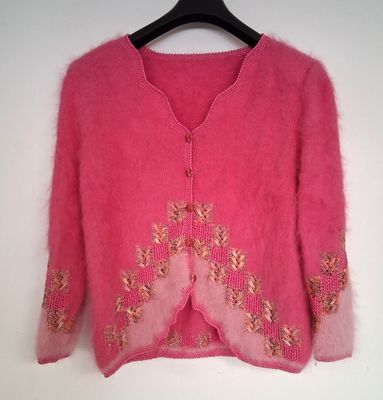 Le pull est rose et orné de broderies dorées.