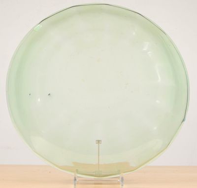 une photo représentant une assiette en verre vert posée sur un socle, elle-même posée sur une table en bois