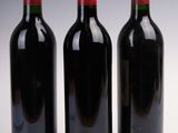 three bottles of red wine sit next to each other on a white surface
