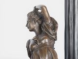 bronze statue of a woman sitting on a stool with her hands on her head