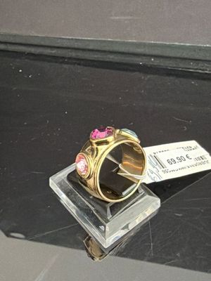une bague en or ornée d'une fleur rose, posée sur un socle en verre