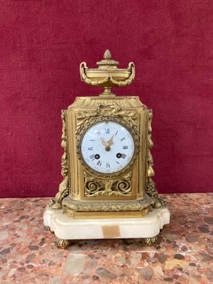 a gold clock on a marble table with a red wall in the background