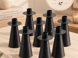 plusieurs bougeoirs noirs posés sur une table, avec une plante en arrière-plan