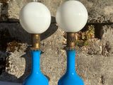 une paire de lampes en verre bleu et blanc posées sur une table devant un mur de briques