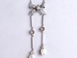a close up of a necklace with pearls and a bow on it