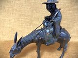 statue en bronze représentant un homme chevauchant une vache, coiffé d'un chapeau