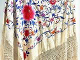 a close up of a white shawl with flowers and fringes