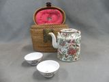 three cups and a teapot sitting next to a basket