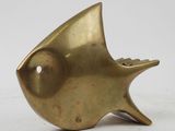 brass sculpture of a fish on a stand on a white surface