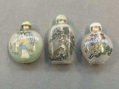 trois flacons à tabac en verre décorés de peintures, posés sur une table