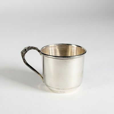 une tasse en argent avec une anse, posée sur une surface blanche