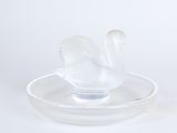 un oiseau en verre transparent posé sur une assiette, sur fond blanc