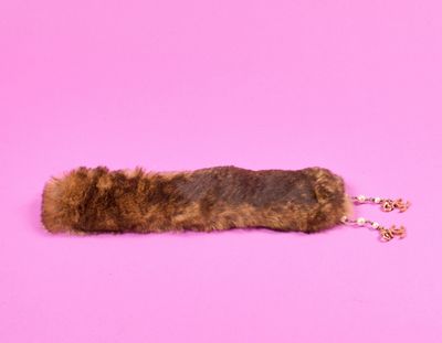 un cache-oreilles en fourrure marron posé sur une surface rose