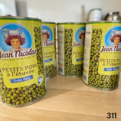 quatre boîtes de petits pois sont posées sur une table, avec une femme en arrière-plan