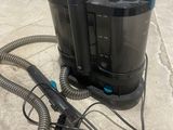 un aspirateur noir et bleu posé par terre à côté d'un tuyau