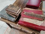 Plusieurs vieux livres sont empilés sur une table en bois, à côté d'une chaise rouge.