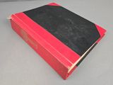 an old red and black book sitting on top of a table