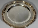 un plat ancien en argent posé sur une table blanche, muni d'une poignée noire