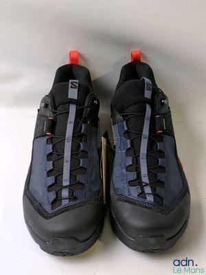 une paire de chaussures de randonnée noires avec des lacets orange sur un fond blanc