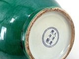 a green vase sitting on a white surface with chinese writing on it