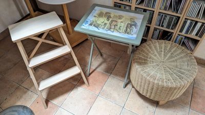 une petite table sur laquelle est posée une photo, avec un tabouret devant une bibliothèque