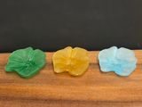three different colored glass flowers sitting on top of a wooden table