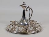a silver plate with a silver pitcher and cups on it