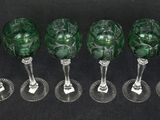 six green glass goblets are lined up on a black surface