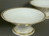 pair of white and gold footed bowls on pedestals against a gray background