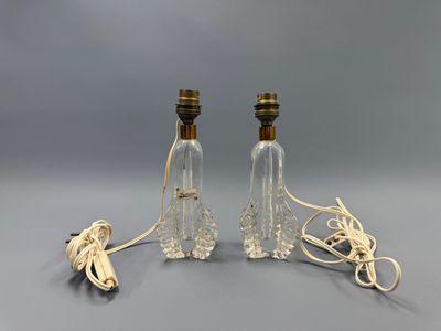 deux lampes en verre transparent posées sur une surface grise, avec un cordon