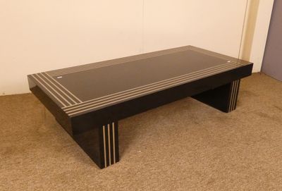 une table basse noire avec un plateau en verre, posée sur un sol recouvert de moquette