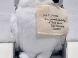 une chouette en peluche blanche posée dans une boîte sur laquelle est accrochée une pancarte