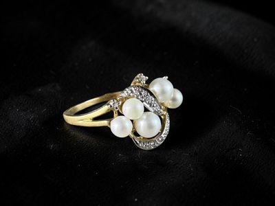 a gold ring with pearls and diamonds on a black background