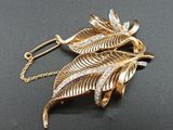 broche en forme de feuille plaquée or, ornée de pierres en cristal, sur une chaîne