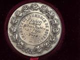 an old silver medal in a velvet case with a red ribbon around it