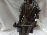 statue en bronze représentant un garçon tenant un marteau, posée sur un tissu blanc