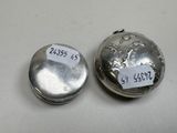 two silver pill cases sitting on top of a table next to each other