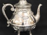silver plated teapot with ornate design on stand on black background