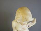 une statue blanche représentant un enfant qui porte ses mains à son visage