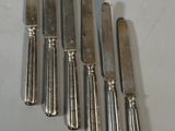 six silverplated knives are lined up on a white surface