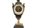 une horloge noire et dorée posée sur un socle, sur fond blanc