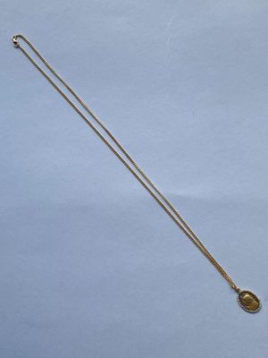un collier en or orné d'une pièce, posé sur une surface bleue