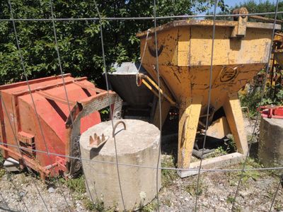 un camion-benne jaune derrière une clôture, à côté d'un conteneur à ciment