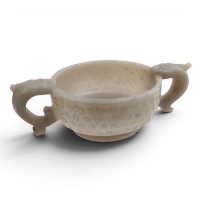 une petite tasse avec une anse posée sur une surface blanche
